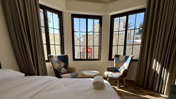 A hotel room with a large bed, two armchairs, a small table, and a view of the outside through large windows. - 1 Antica jabalal-lwebdeh (Amman)
