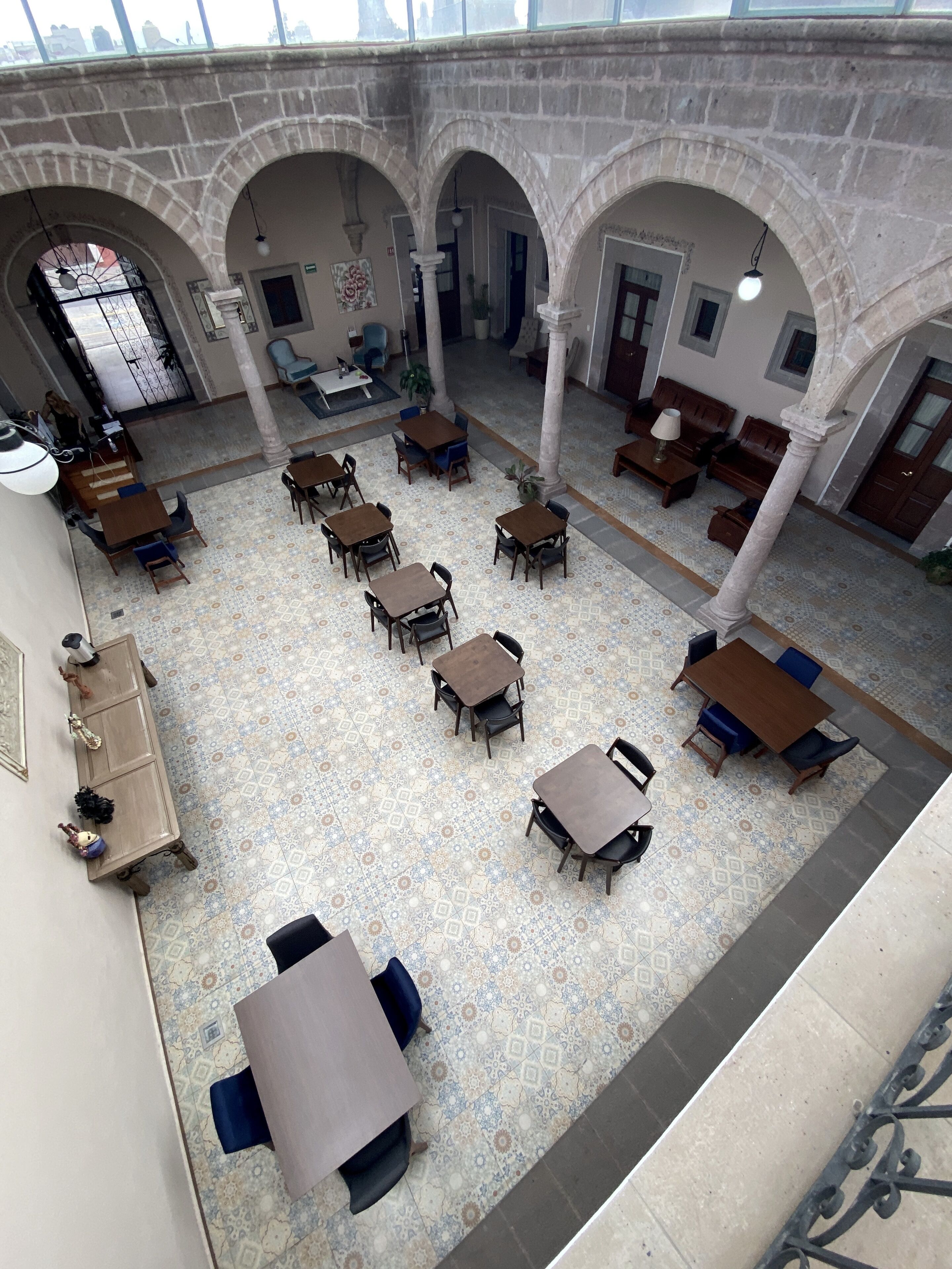 A spacious indoor area with multiple tables and chairs arranged in a courtyard-like setting, featuring stone arches and a tiled floor.