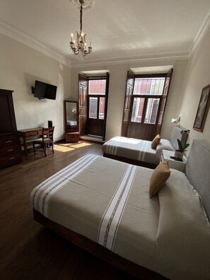 A bedroom with a large bed, a desk, a chair, a television, and a window with a view of the outside. - Cantera Real Hotel (Morelia)