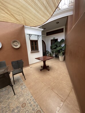 A spacious patio area with a wooden table and chairs, surrounded by potted plants and a large window. - Cantera Real Hotel (Morelia)