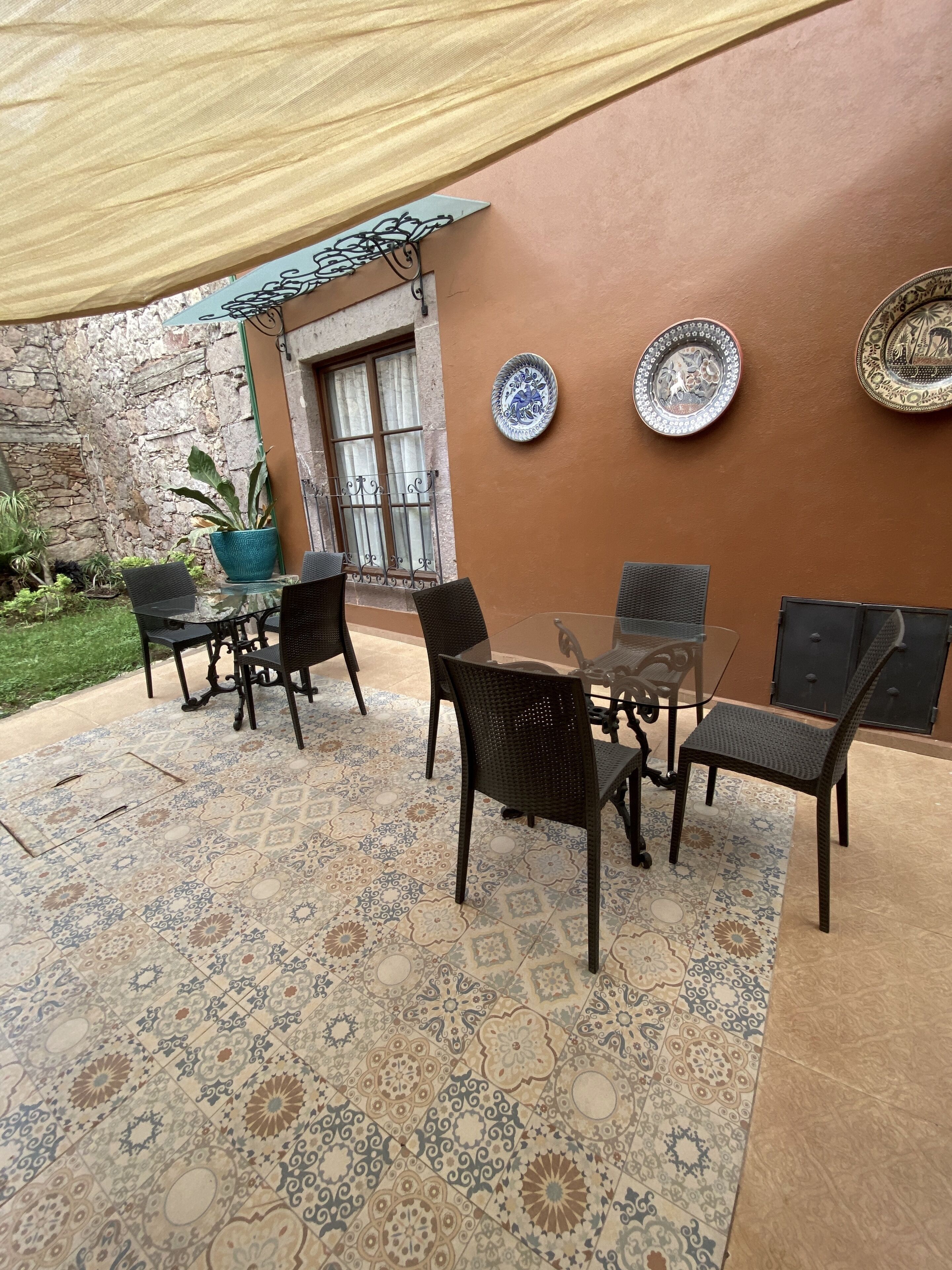 Un patio al aire libre con una mesa y sillas, platos decorativos en la pared y una planta en maceta.
