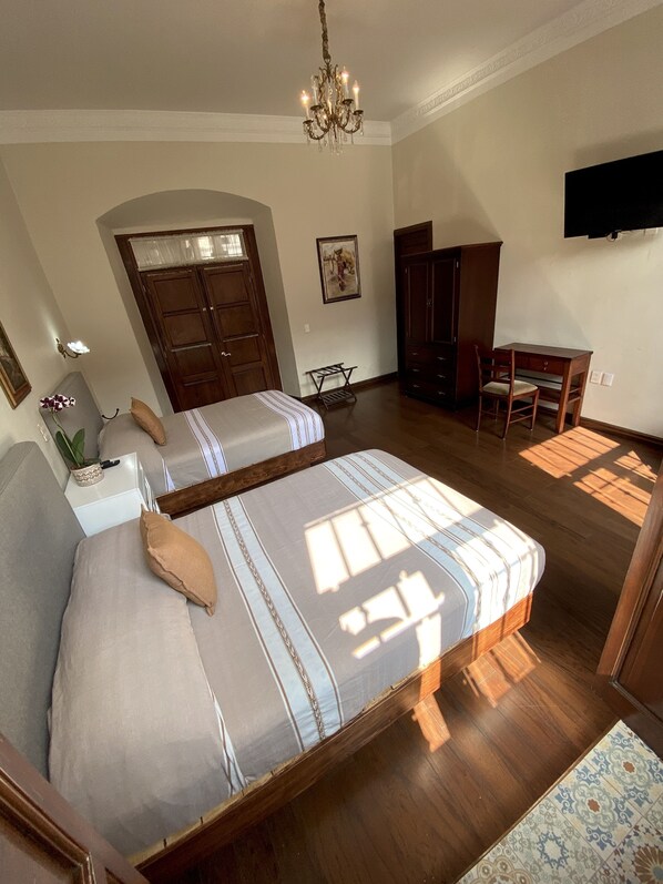 A bedroom with two beds, a desk, a chair, a TV, and a chandelier. - Cantera Real Hotel (Morelia)