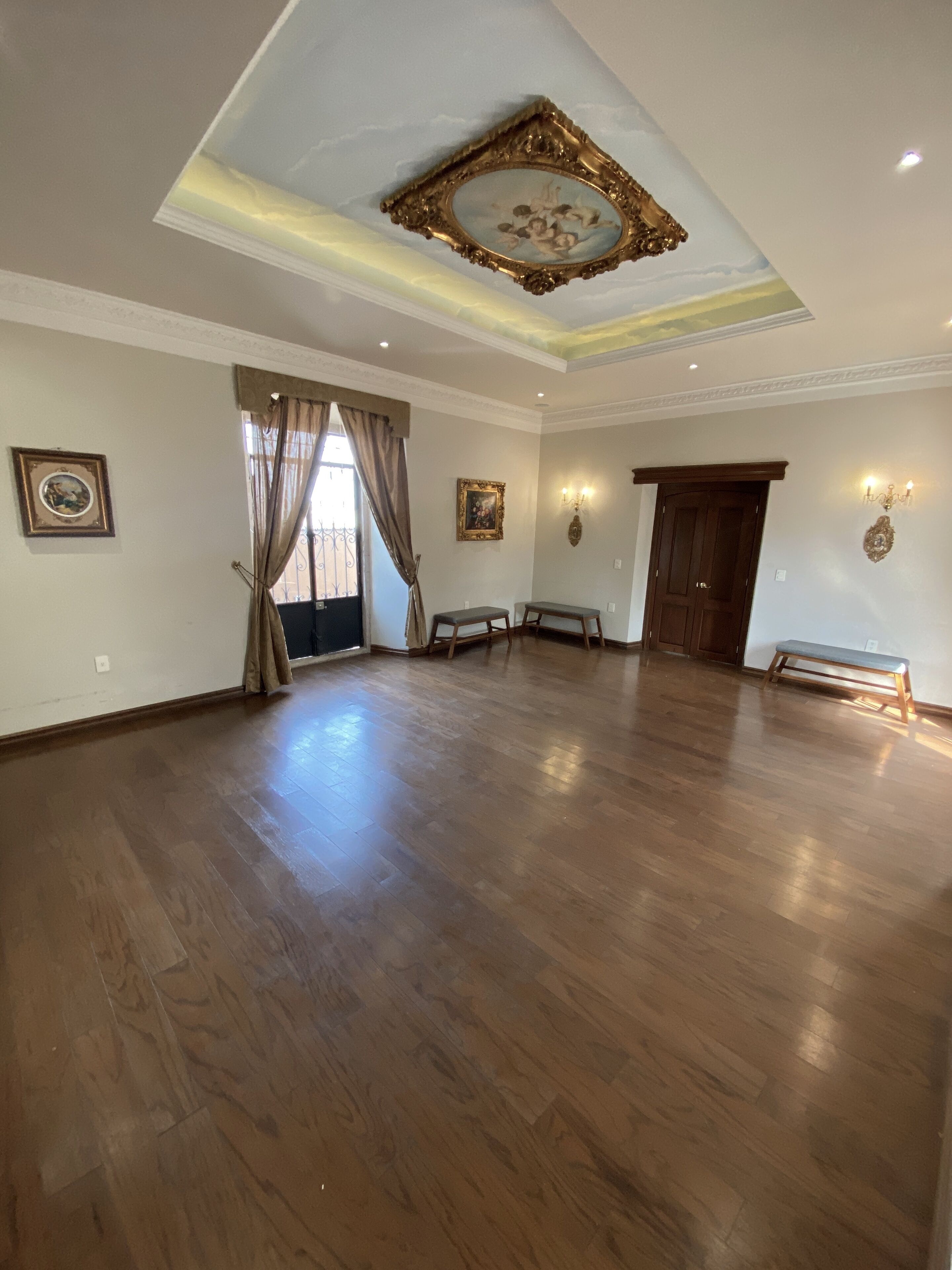 Un'ampia stanza con pavimento in legno, un grande specchio e un soffitto con decorazioni.