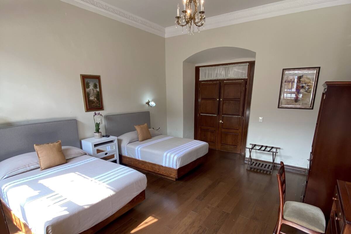 Un dormitorio amplio con dos camas, un candelabro, piso de madera y un gran arco de entrada.