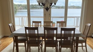 A dining area with a table and chairs, a chandelier, and large windows with a view of a lake. - WATER FRONT- saltwater private pond beach and water sports IDEAL for big groups! (Dennis)
