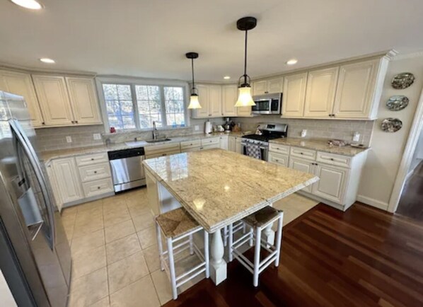 A modern kitchen with white cabinets, a large island with bar stools, stainless steel appliances, and pendant lighting.