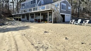 A two-story house with a covered porch and a sandy beach in front. - WATER FRONT- saltwater private pond beach and water sports IDEAL for big groups! (Dennis)