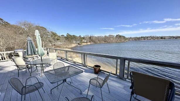 A deck with outdoor furniture, a table, and chairs overlooking a body of water. - WATER FRONT- saltwater private pond beach and water sports IDEAL for big groups! (Dennis)