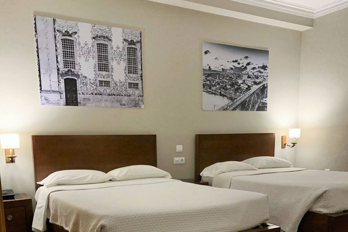 Habitación de hotel con dos camas individuales, suelo de madera y dos mesitas de noche fijadas a la pared con lámparas.