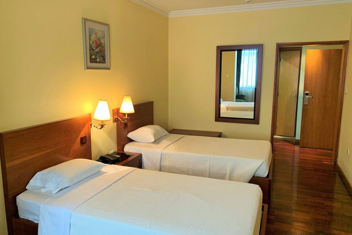 Habitación de hotel con dos camas, una mesita de noche, una lámpara, un espejo y una puerta.