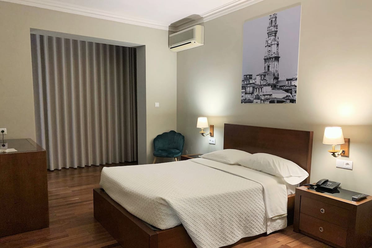 Habitación de hotel con cama, lámparas de noche, escritorio con teléfono y aire acondicionado instalado en la pared.