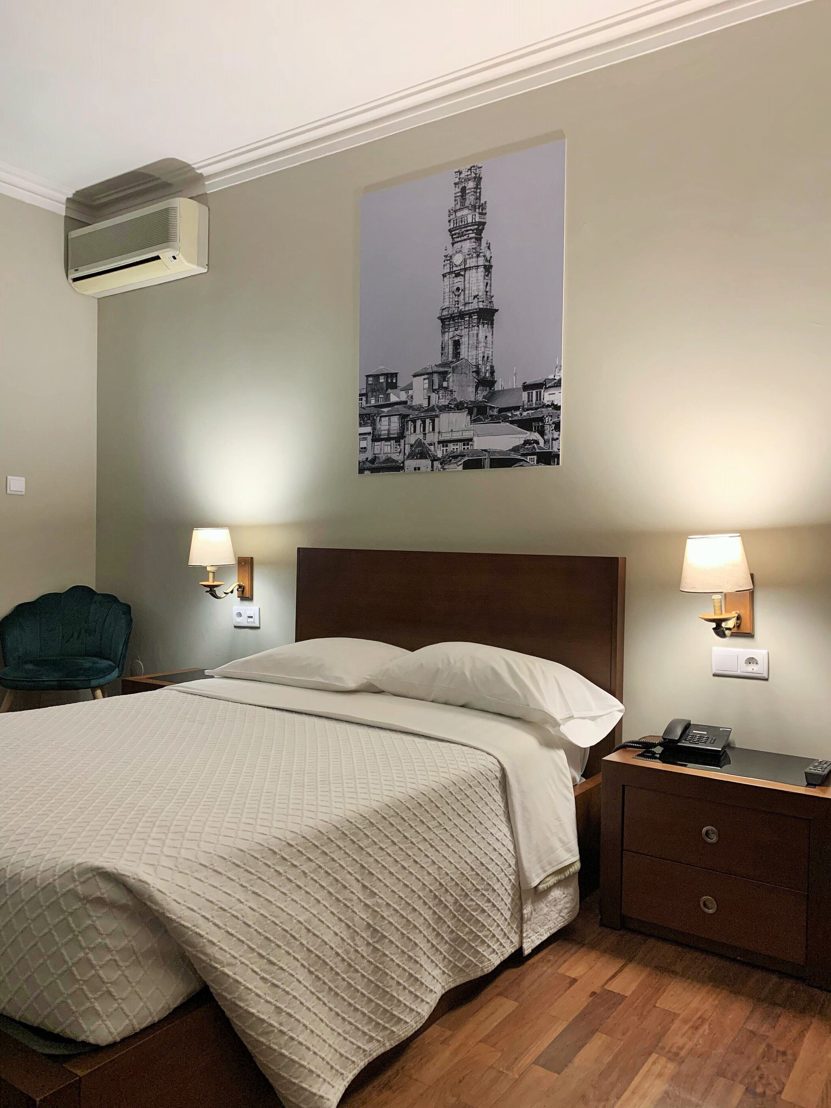 Une chambre d’hôtel comprenant un lit, deux lampes de chevet, une table de chevet avec un téléphone, une chaise et un climatiseur fixé au mur.