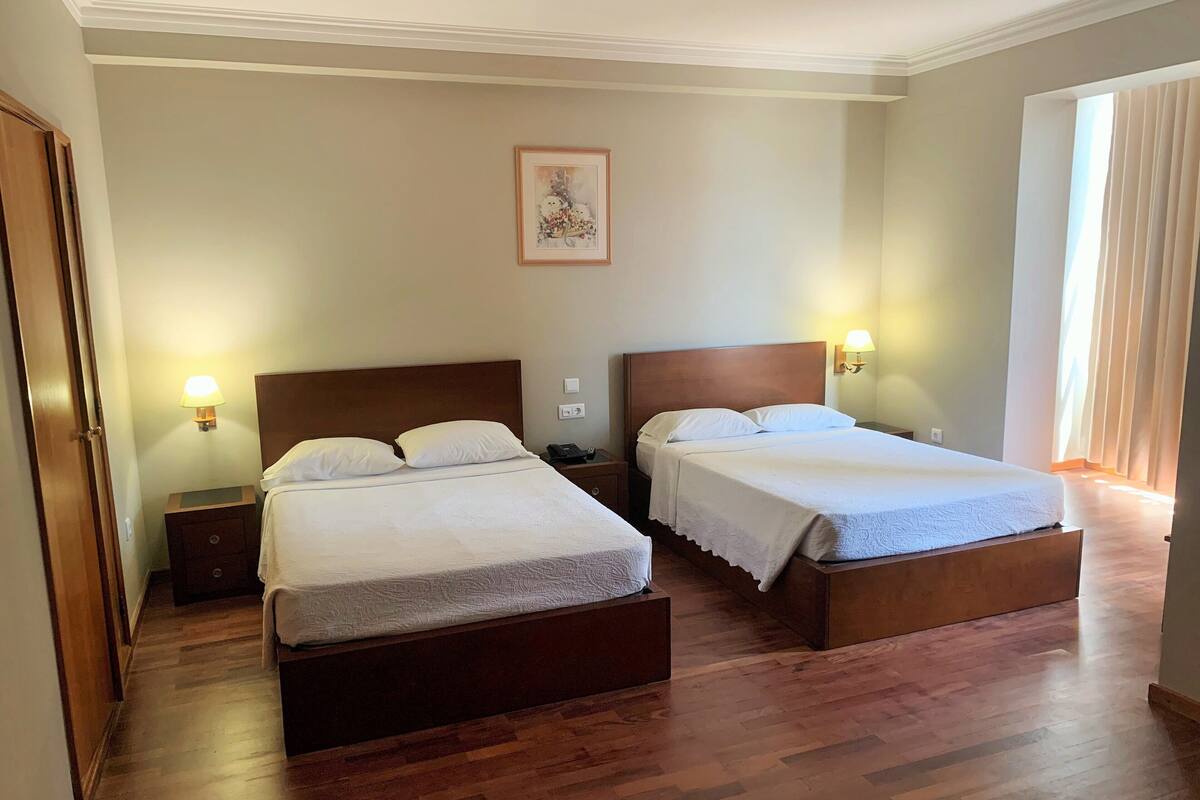 Una habitación de hotel con dos camas de madera, una mesita de noche con una lámpara, un cuadro enmarcado en la pared y piso de madera.