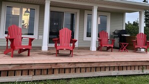 A two-story house with a covered porch, red Adirondack chairs, and a grill.