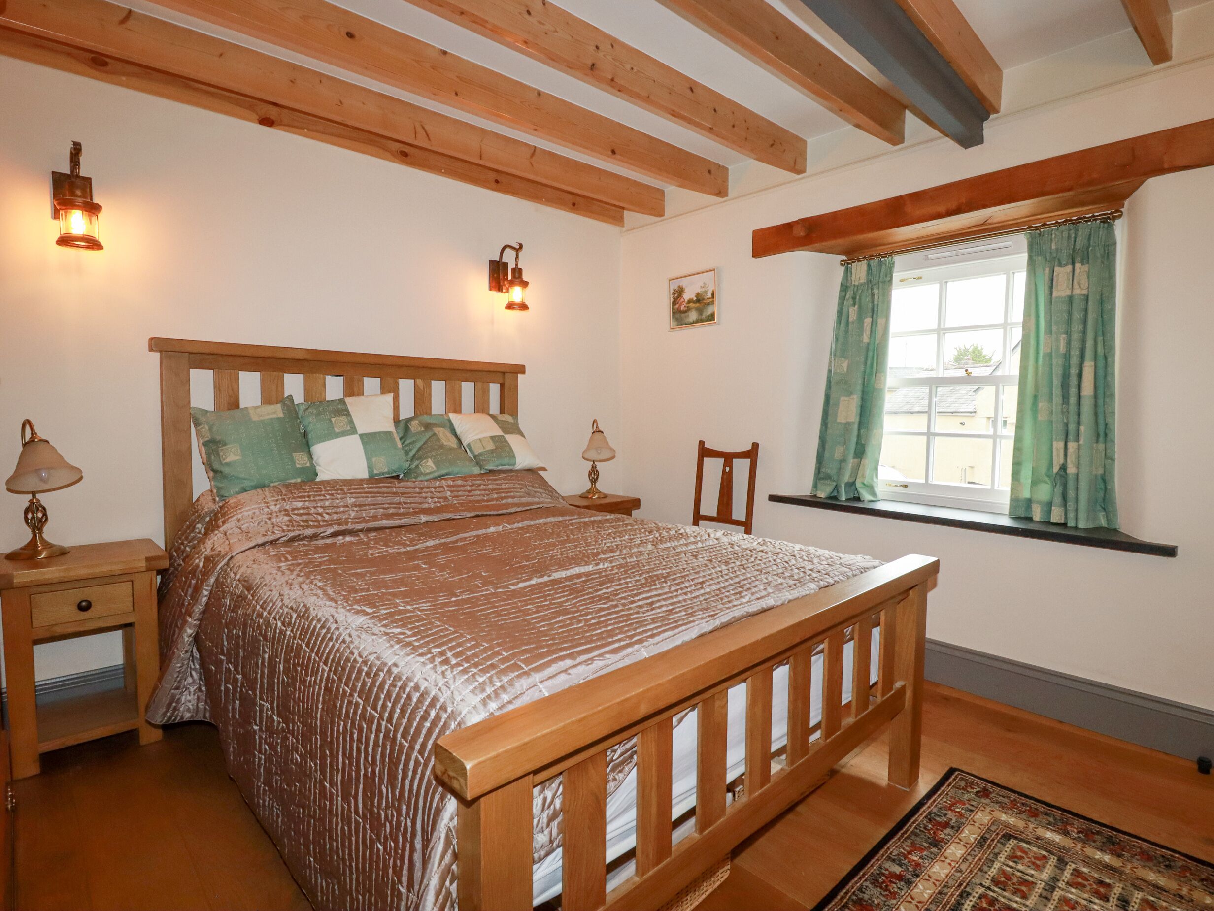 Een slaapkamer met een houten bed, twee bedlampen, een raam met gordijnen en een klein schilderij aan de muur.