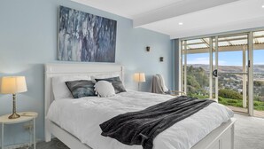 Una camera da letto con un letto grande, due comodini con lampade, un quadro appeso e vista panoramica tramite una porta vetrata.
