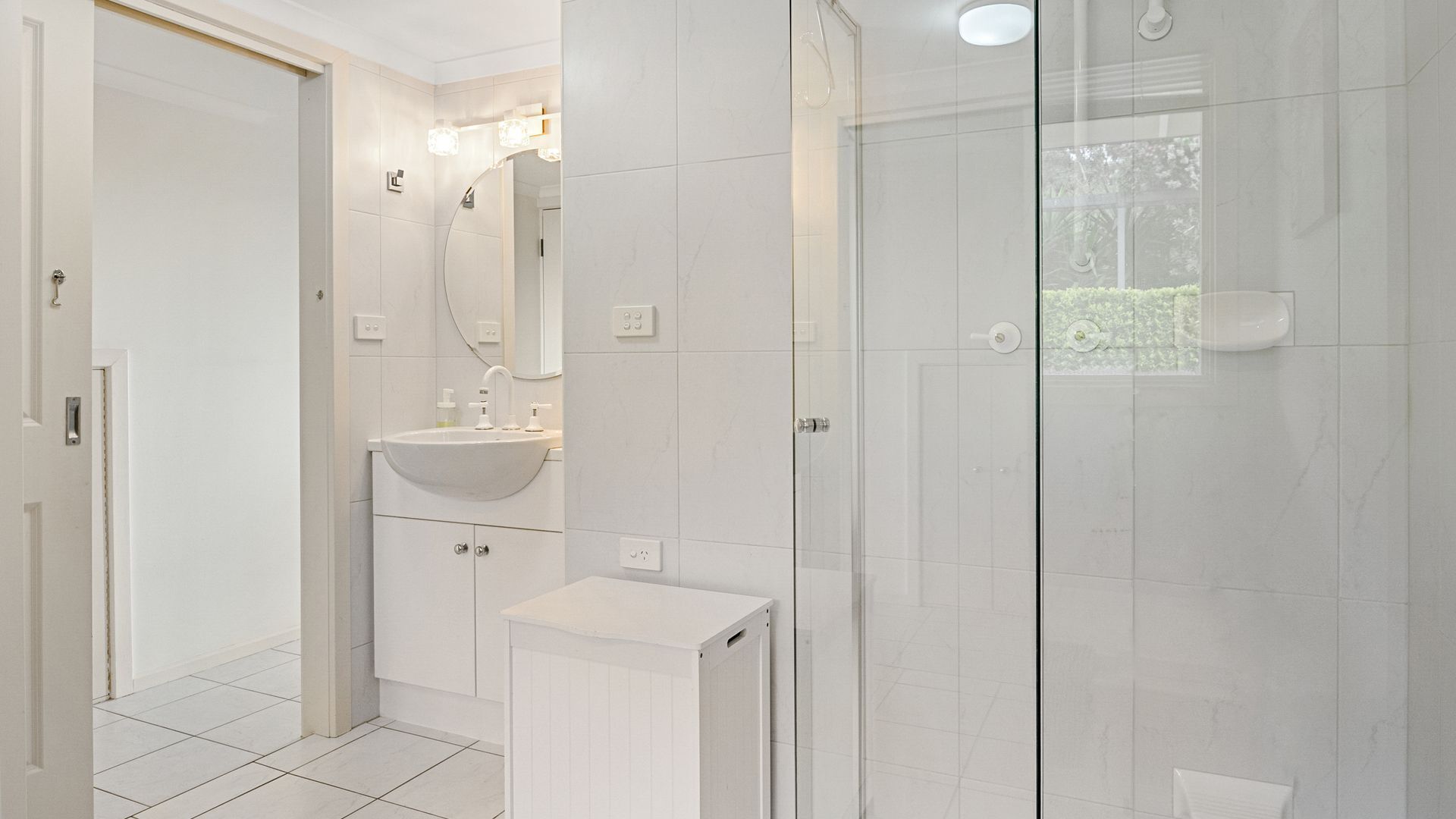 Un baño moderno con cabina de ducha de vidrio, un lavamanos blanco y un espejo encima.