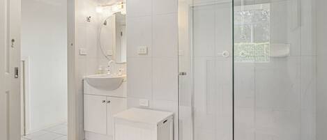 Un baño moderno con cabina de ducha de vidrio, un lavamanos blanco y un espejo encima.