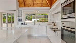 Una cucina moderna con mobili bianchi, un piano di lavoro in marmo, forno integrato e vista sul giardino attraverso ampie finestre.