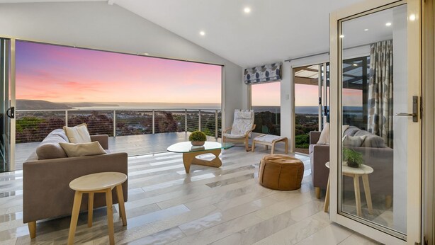 Un ampio balcone con vista sull'oceano al tramonto, arredato con un divano, sedie e un tavolino.