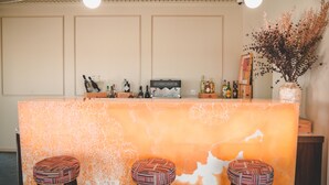 Una zona de bar con encimera de mármol, tres taburetes, una máquina de café y un florero con flores secas.