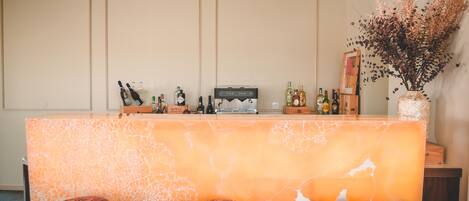 A bar area with a marble countertop, three stools, a coffee machine, and a vase of dried flowers.