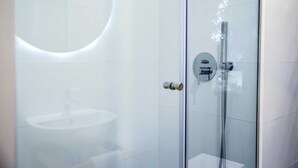 Un baño moderno con ducha de vidrio, espejo redondo y lavamanos blanco.
