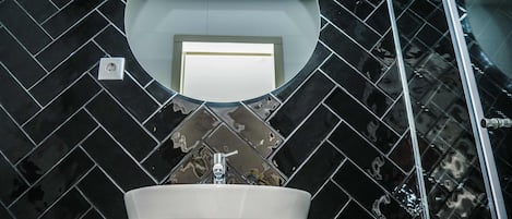 A bathroom with a black tiled herringbone pattern, a white sink, a mirror, and a glass shower enclosure.