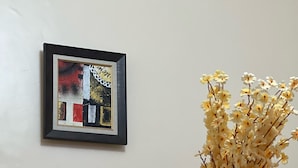 Un tableau abstrait encadré accroché au mur, un vase contenant des fleurs séchées et un petit bol en verre rempli de perles colorées.