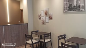 Un espace repas comprenant deux tables et quatre chaises, un mur orné de tableaux encadrés et un comptoir d’accueil en bois.