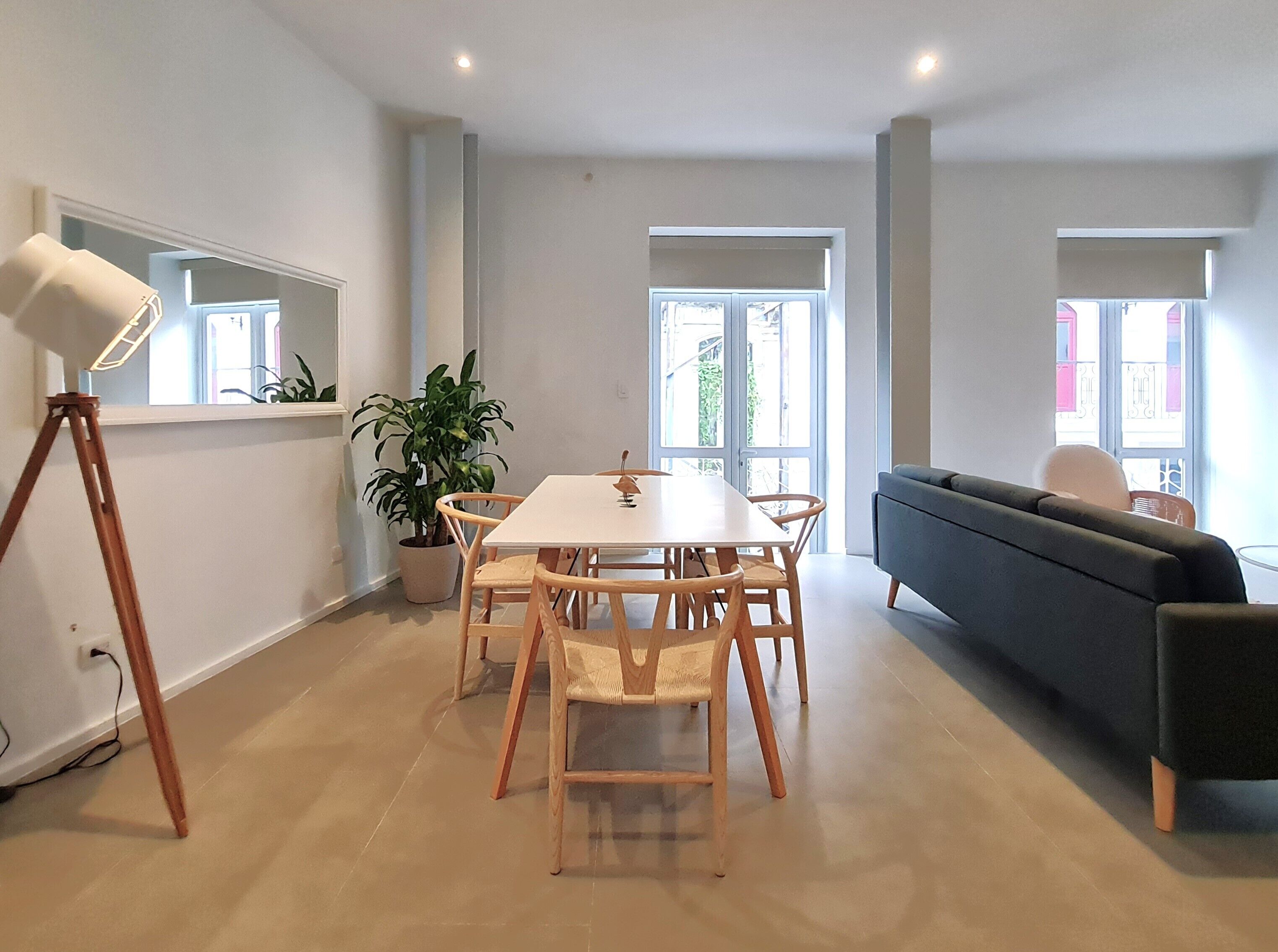 Un salon moderne comprenant une table à manger, des chaises, un canapé, une plante en pot et un lampadaire sur trépied.