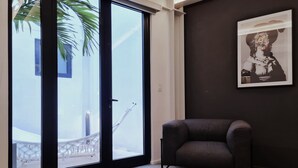 Una habitación con puerta corrediza de vidrio que da a un balcón, un sillón oscuro y un cuadro en la pared.