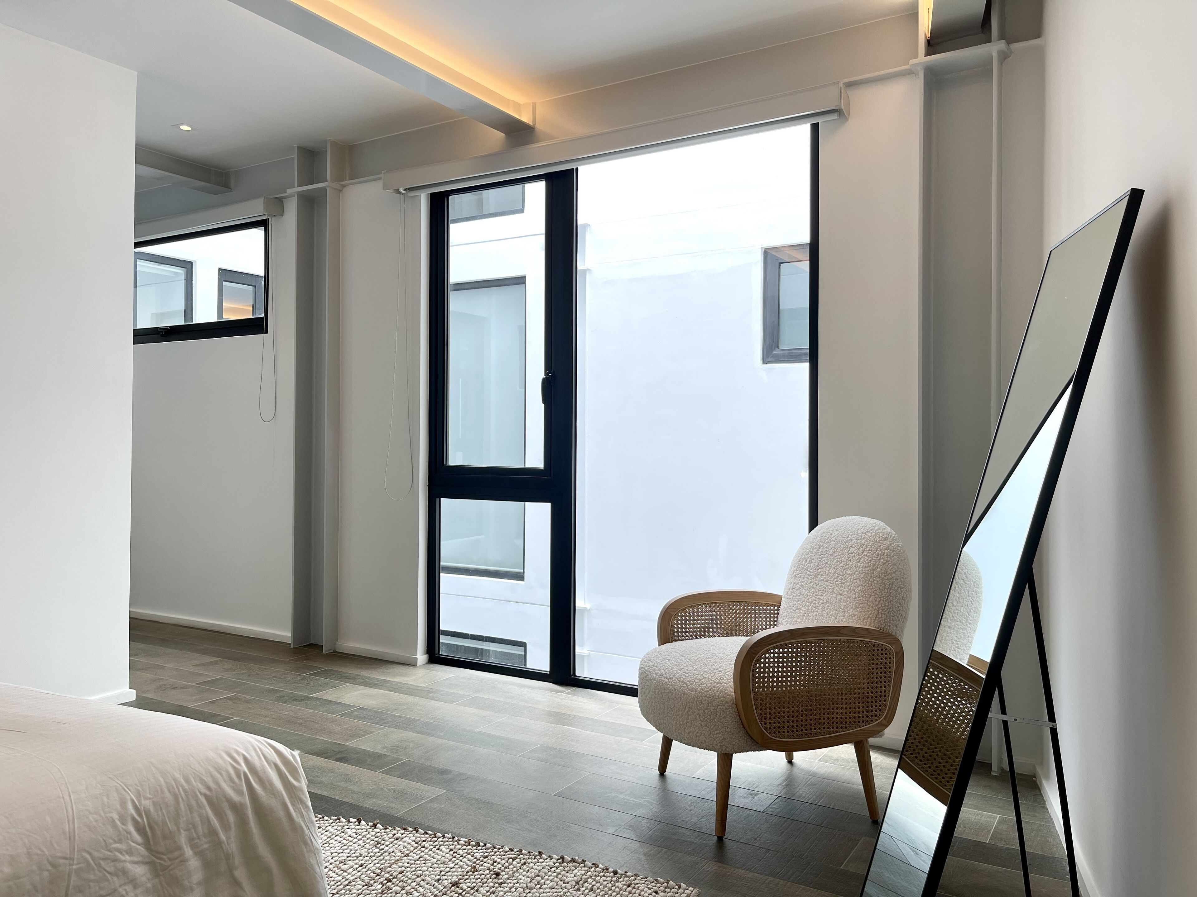 A modern room with a large sliding glass door leading to a balcony, a bed with a white duvet, and a wicker chair.