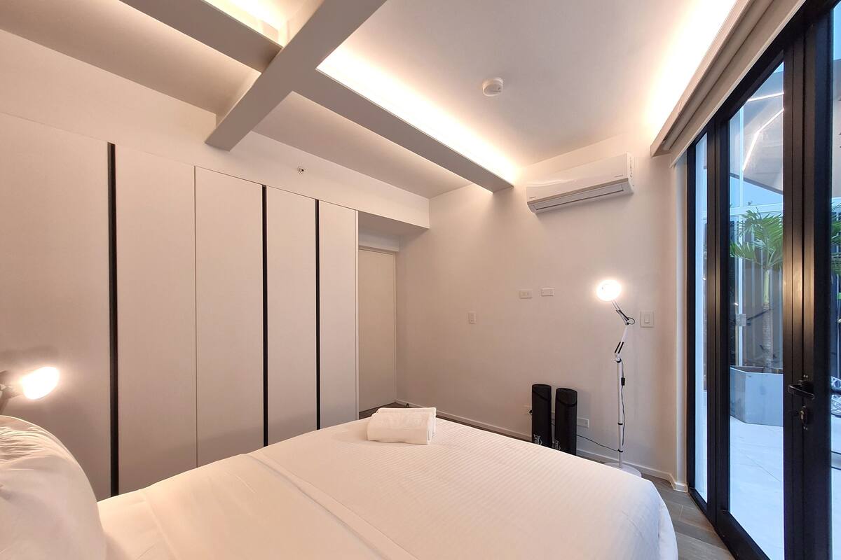 Ein modernes Schlafzimmer mit einem großen Bett, Einbauschränken, einer Stehlampe und Blick durch eine Glastür.