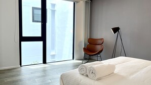 Habitación de hotel con cama, una silla, una lámpara de pie y un ventanal corredizo al exterior.