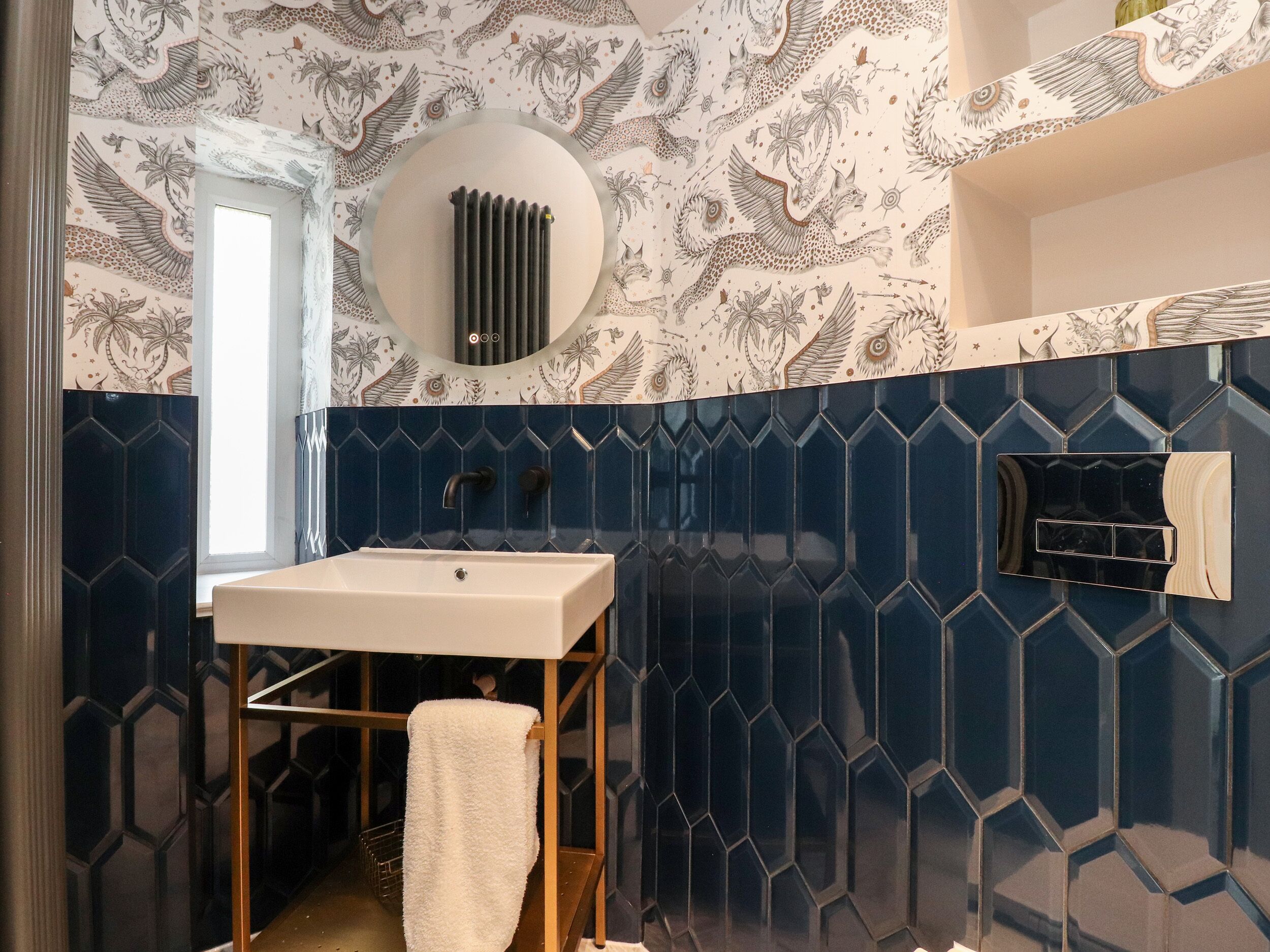 Een badkamer met een wit wastafel, donkerblauwe hexagontegels, een handdoekhouder en een radiator.
