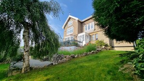 A two-story house with a stone pathway leading to the entrance, surrounded by lush greenery and a well-maintained lawn.