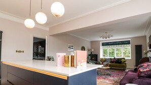A modern kitchen with a central island, a dining area with a sofa and a coffee table, and a view of the outdoors through a window.