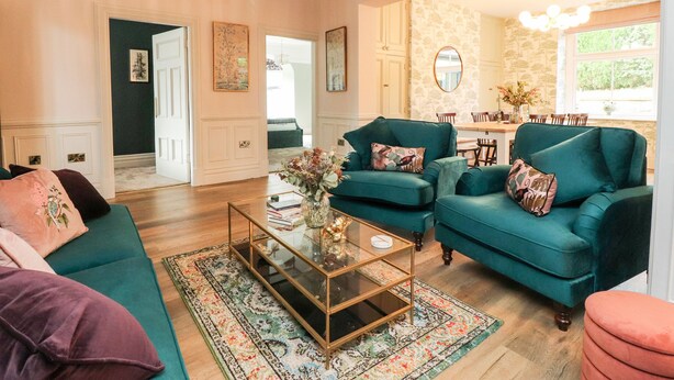 A spacious living room with teal sofas, a glass coffee table, and a chandelier.