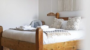 A neatly made bed with a wooden headboard, a hanging light fixture, and a macramé wall hanging. - La Casita - 2-bed House in Newquay (Newquay)