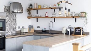 A modern kitchen with a central island, built-in appliances, and open shelving with decorative items. - La Casita - 2-bed House in Newquay (Newquay)