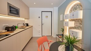 A modern kitchen with a microwave, toaster, and coffee maker. There is a door with a sign, a small table with a plant, and a chair. - New apartment Central Station Milan (Milano)