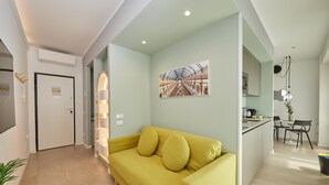 A modern living room with a yellow sofa, a dining area with a small table and chairs, and a kitchen with a countertop and cabinets. - Circular Apartment . (Milano)