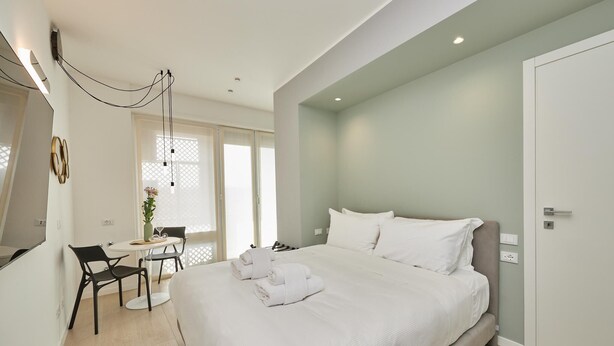 A modern hotel room with a large bed, a desk with two chairs, and a small table with a vase of flowers. - Circular Apartment . (Milano)
