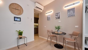 Un intérieur moderne avec une horloge murale ronde en bois, une petite table avec une plante, deux chaises disposées autour d’une table ronde et un climatiseur fixé au mur.