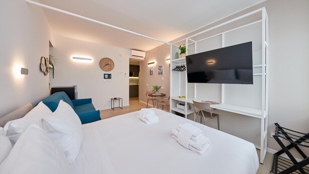 Une chambre d’hôtel moderne dotée d’un grand lit, d’un téléviseur fixé au mur blanc, d’un petit bureau et d’un coin salon avec une chaise et une table.