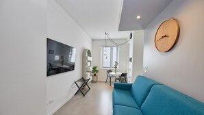 A modern living room with a blue sofa, a wooden clock, and a dining area with a table and chairs. - Luxury apartment in the center of Milan - NEW (Milano)