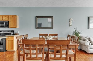 A dining area with a wooden table and chairs, a kitchen with wooden cabinets, a microwave, and a stove.