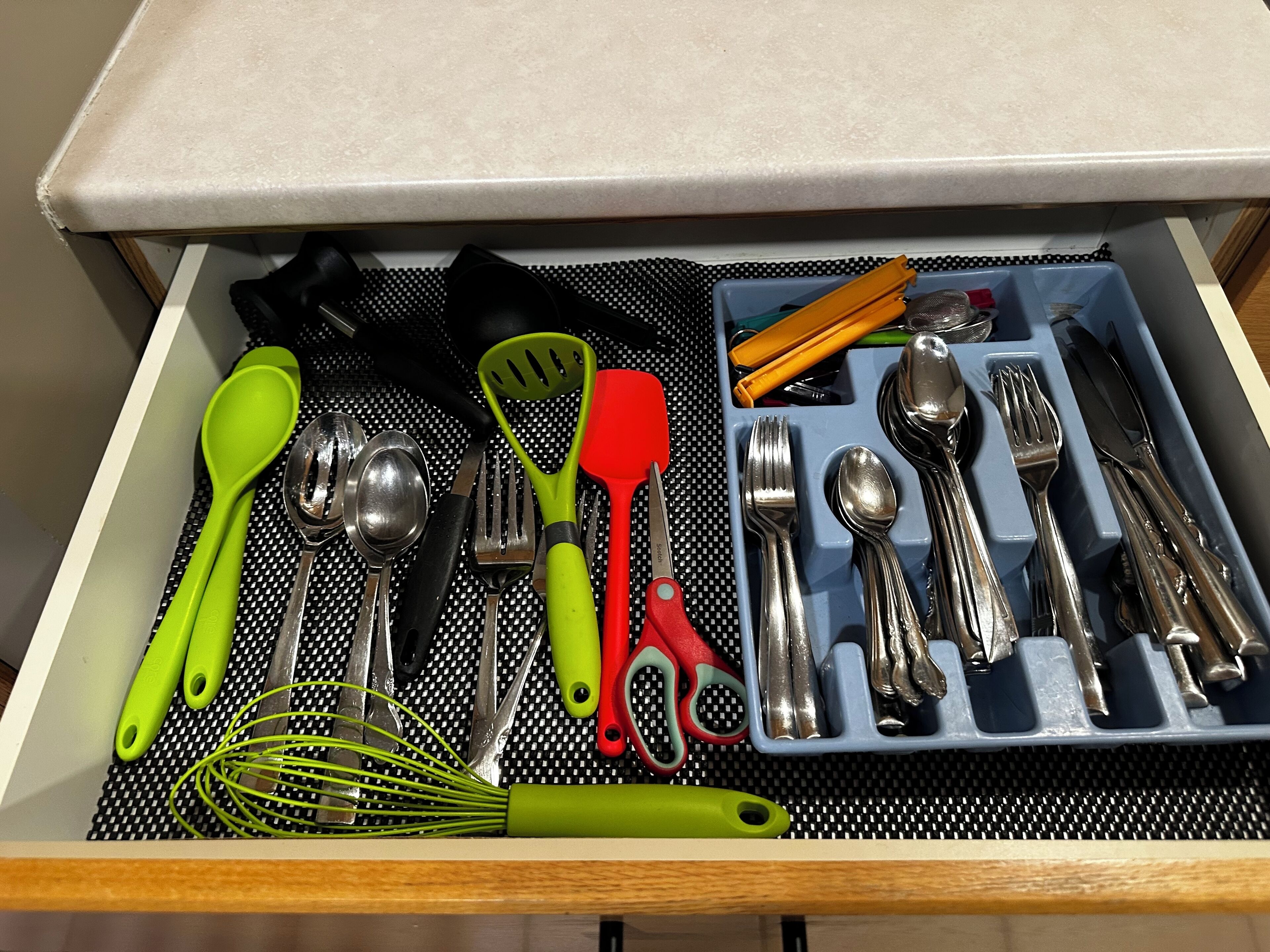 Un cajón con varios utensilios y herramientas de cocina, incluyendo cucharas, tenedores, cuchillos y un batidor.