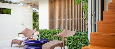 Un espace extérieur moderne, aménagé avec des chaises en osier et une table bleue, entouré de verdure et délimité par une clôture en bois.